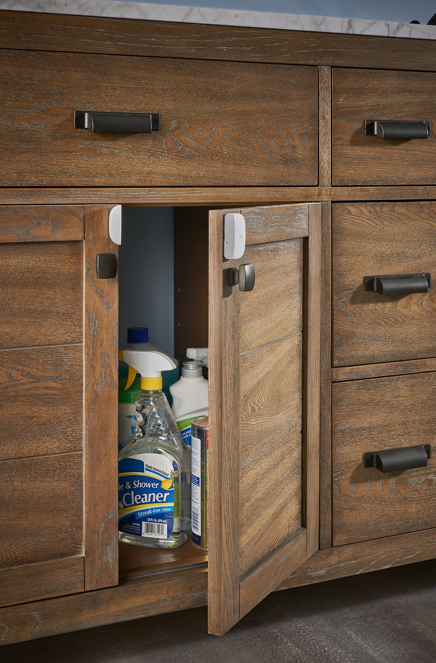 SmartThings Multipurpose Sensor installed on a sink cabinet door that's slightly open, showing cleaning supplies inside