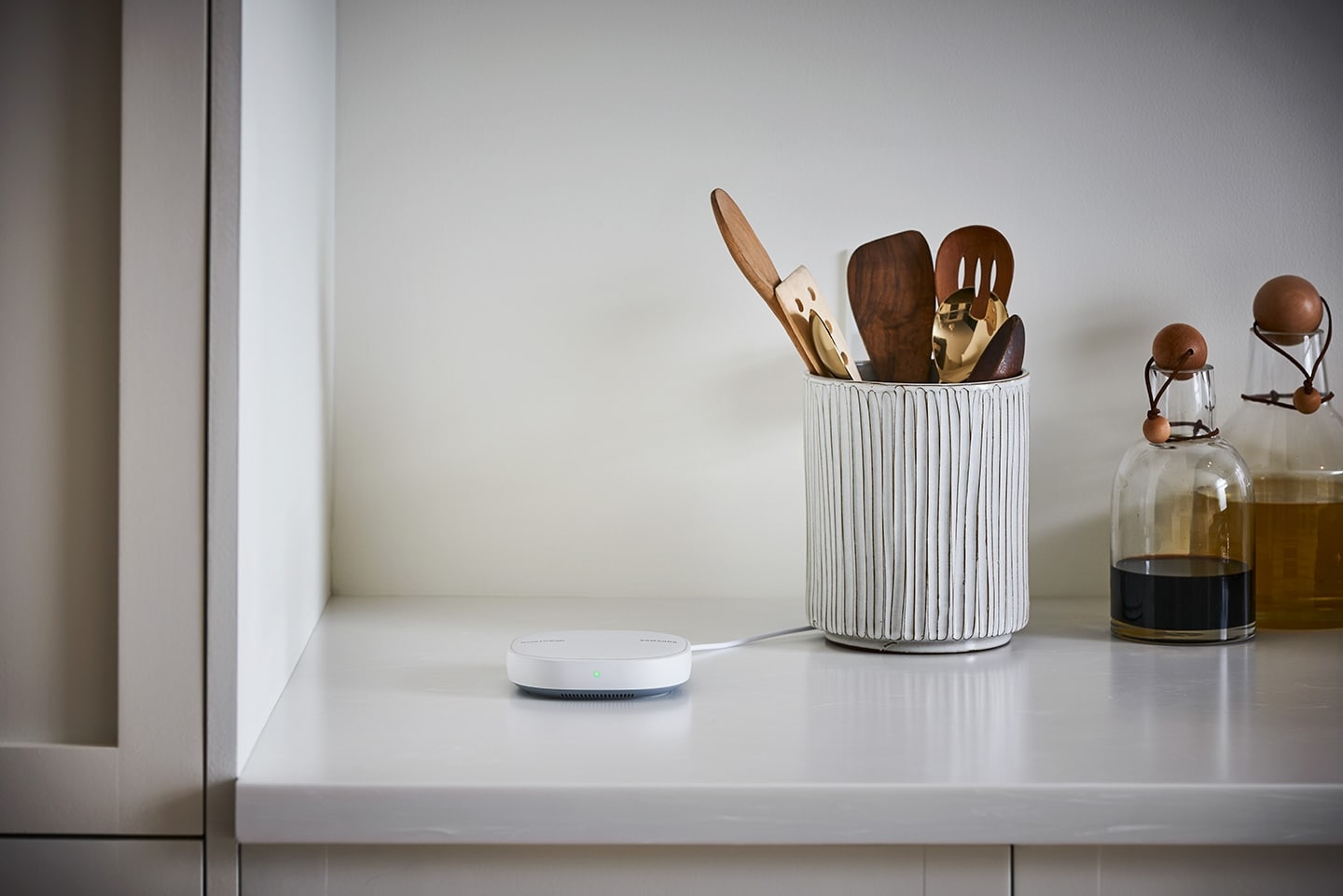 Samsung SmartThings Hub on a Kitchen counter Next to Olive Oil, Balsamic Vinegar Containers and a Tub of Utensils
