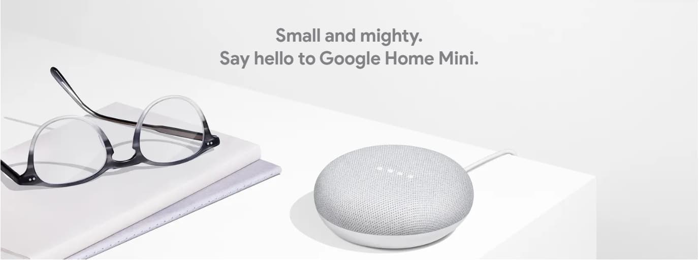 Google Home Mini placed alongside a pair of glasses and two notebooks