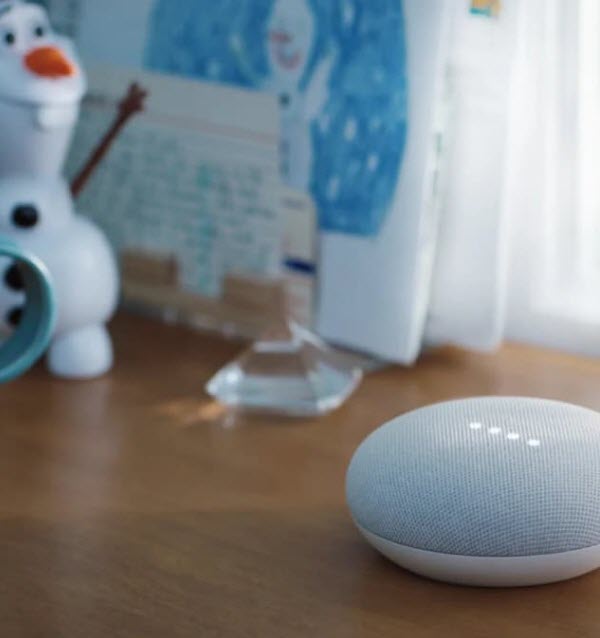 Google Home Mini placed on a wooden desk alongside an alarm clock
