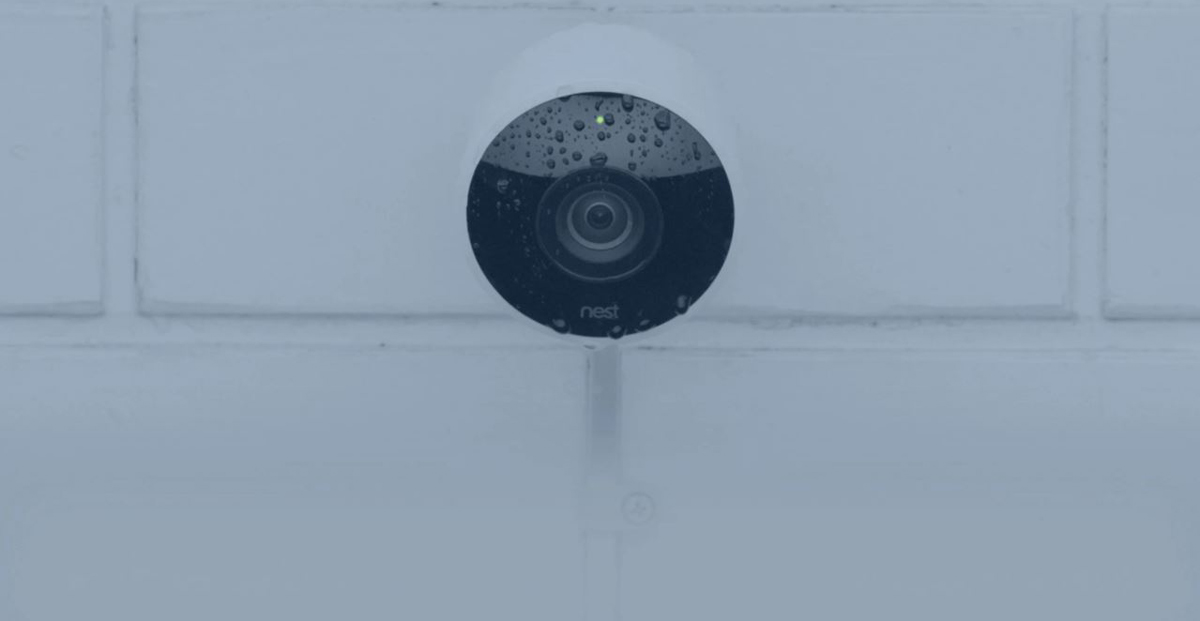 A Google Nest Cam Outdoor camera on the exterior wall has water spots all over its front face.