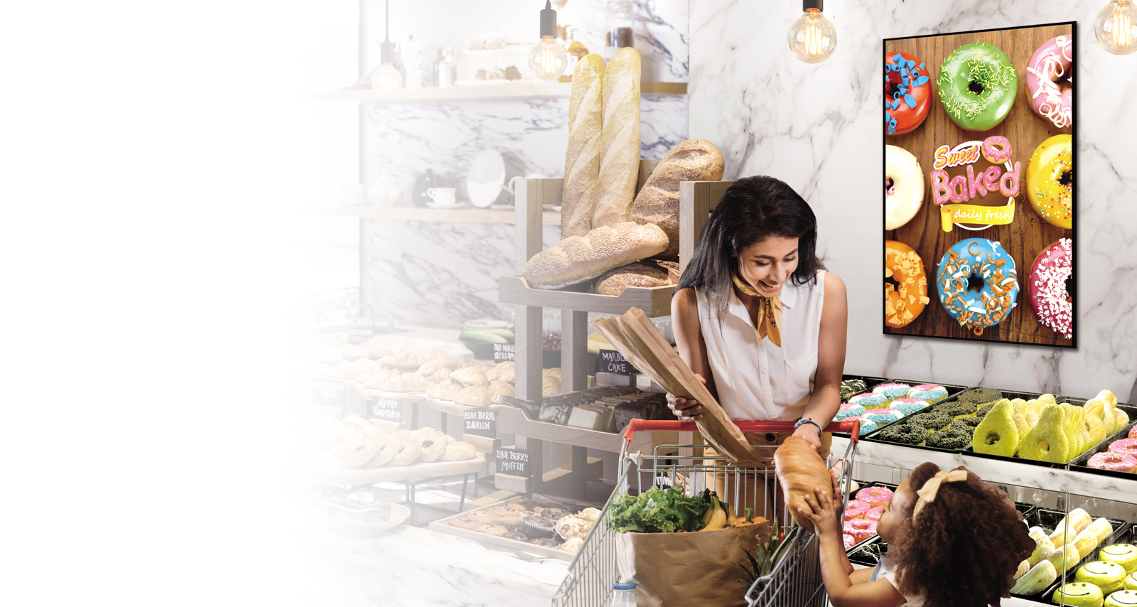 LG display mounted horizontally showing an ad of donuts in a bakery where a mom and daughter are shopping
