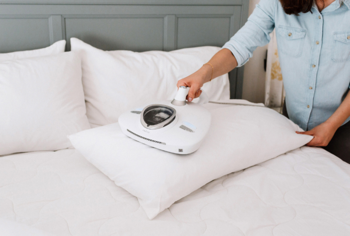 a woman using her RAYCOP VCEN-100USWH vacuum on her pillow