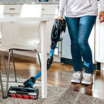 A Woman Using the Shark IF200W on a Rug Under a Chair in Reach Mode