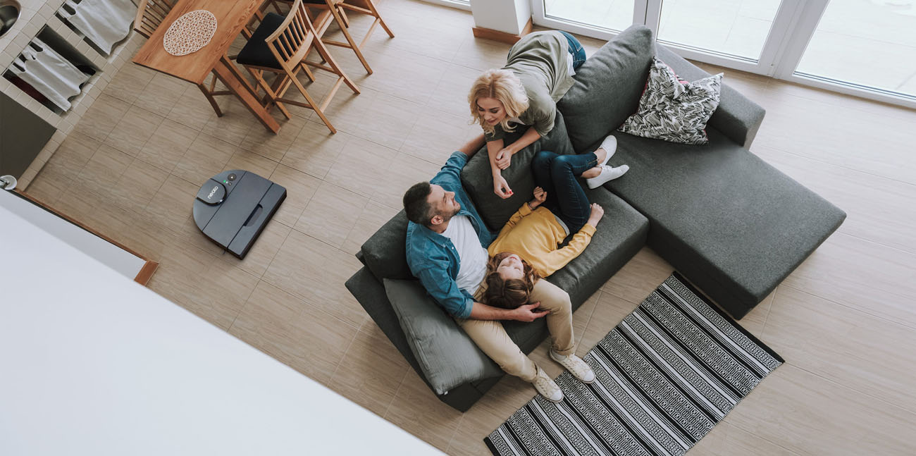 A family of thrre is talking while Neato D8 is working on the floor.