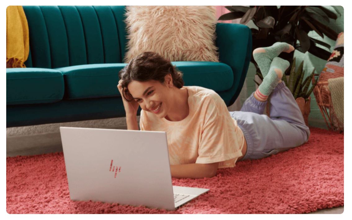 A girl is using a HP laptop while being on his belly.