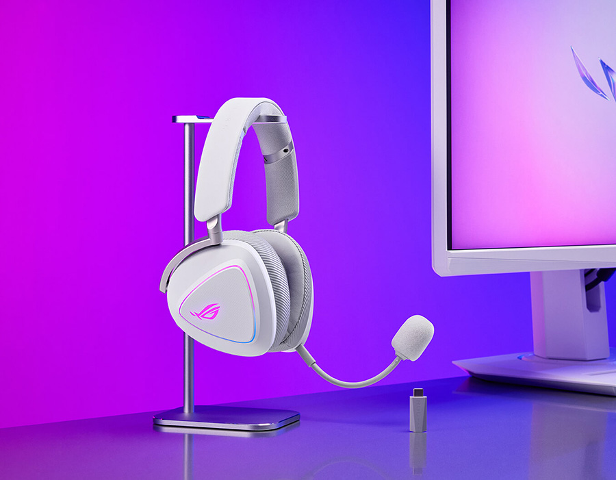 Gaming setup with ROG monitor, keyboard, mouse, ROG Carnyx microphone and ROG Delta II Moonlight White Edition headset on a stand under purple-blue lighting