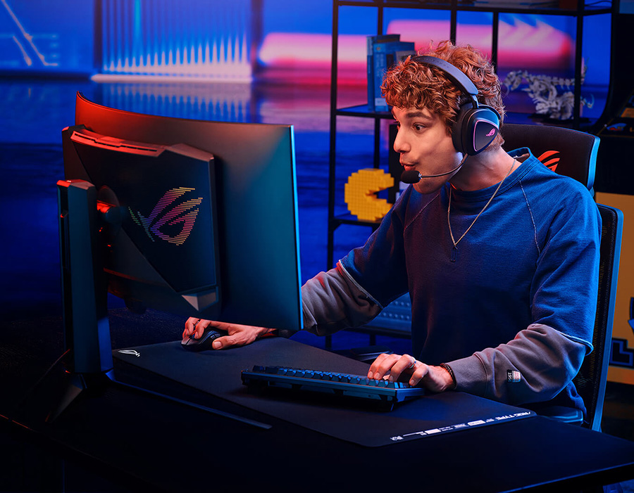 A man wearing the ROG Delta II with microphone, intensely focused on a ROG monitor while holding a gaming mouse and keyboard