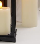 Lit white pillar candle in a black metal lantern holder, placed on a white surface.