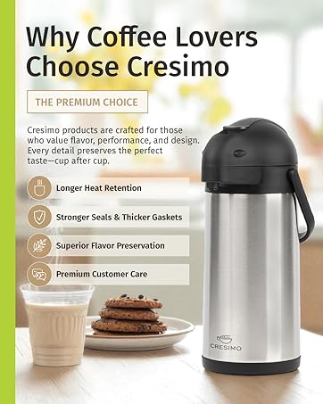 A Thermal Coffee Airpot on a wooden table next to a plate of chocolate chip cookies and milk