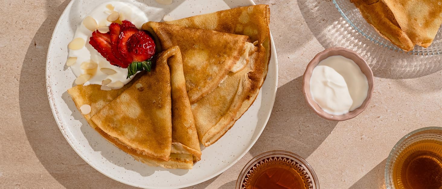 three pancakes with strawberries and cream on a plate.