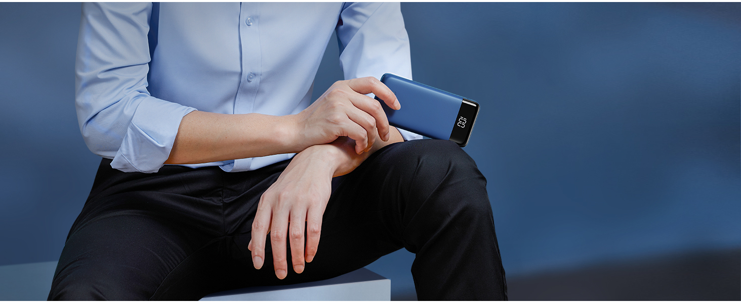 A person wearing a blue shirt holds a navy blue smartphone, demonstrating its use while seated. The phone appears slim and modern.