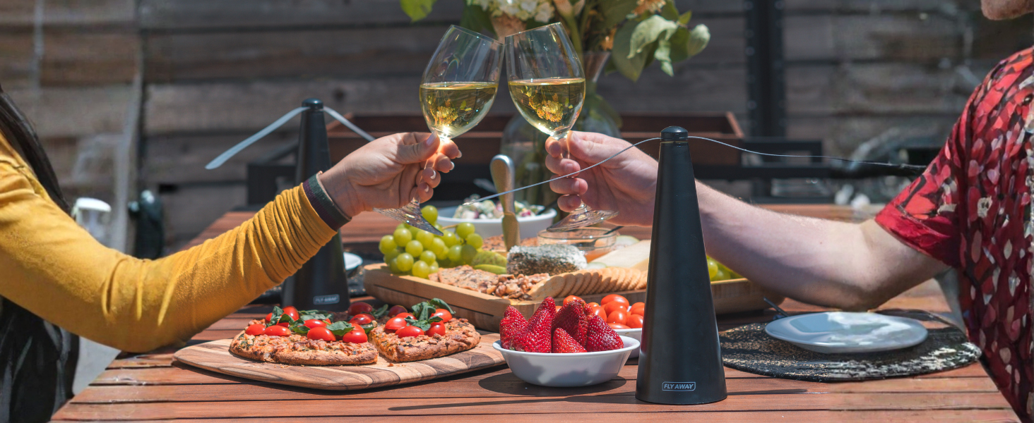 Couple toasting outdoors with food on the table and Fly Away fans keeping flies away during dining.
