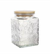 Square glass jar with embossed flower design. Clear glass body with a gold-colored screw-on lid. Suitable for storage or decorative purposes.