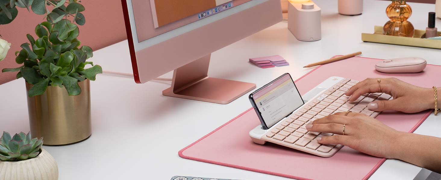 a woman typing on k585 slim compact wireless rose keyboard with phone holder
