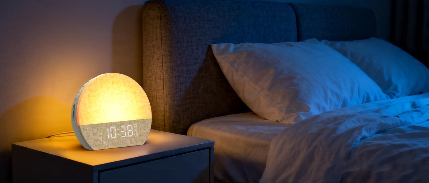 Bedside scene with warm golden-yellow spherical alarm clock glowing on dark wooden nightstand, adjacent to blue decorative pillow on bed in dim bedroom lighting.