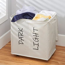 filled cream fabric divided laundry hamper, labeled dark and light in corner, gray wall, wood floor