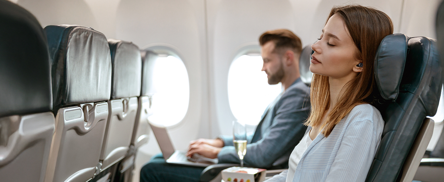Interior view of airplane cabin showing passengers using laptops and devices while seated.