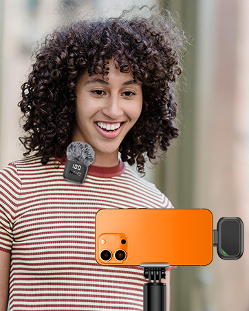 Person wearing red and white striped shirt holding orange rectangular device with dual black speakers against torso, demonstrating portable audio equipment.