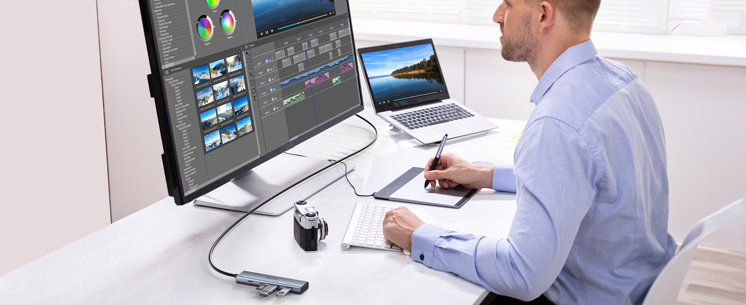 Professional desk setup showing dual monitor workstation with graphic design software open, drawing tablet, and laptop for digital content creation.