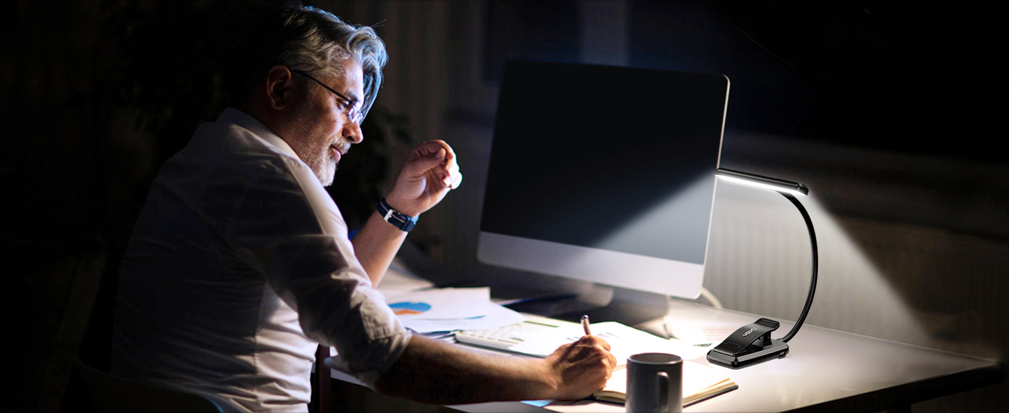 Person working late at night on a laptop in a dark room. Desk lamp illuminates the workspace, creating a focused atmosphere.