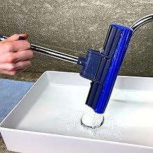 a hand holding a blue and silver faucet over a white sink.