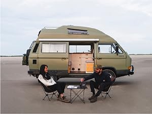 Photo of people relaxing at a table set up outside their camper van in nature