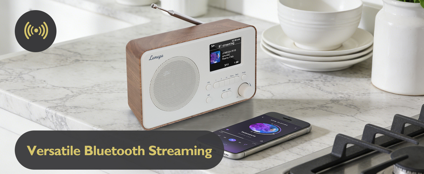 Text reads 'Versatile Bluetooth Streaming'. Digital radio with wooden-finish sides and color display screen shown on kitchen counter next to smartphone.