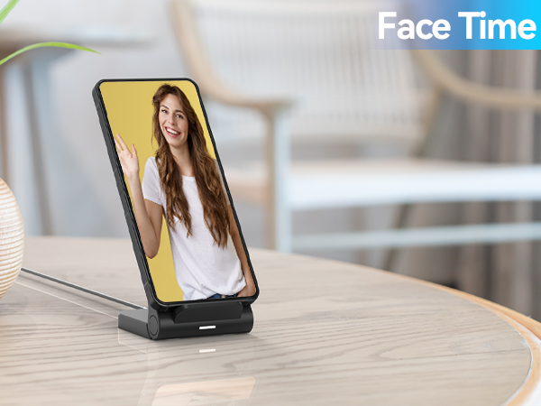 Smartphone on vertical charging stand displaying video call interface. Device shows full-screen image on yellow background. 'Face Time' text overlay in corner.