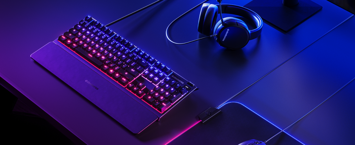 - A SteelSeries desk setup with Apex keyboard, Rival 3 mouse, Arctis headset, and QcK Prism mousepad