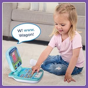 Girl pushes W button on toy laptop. Toy laptop says: W! www. Wagon!