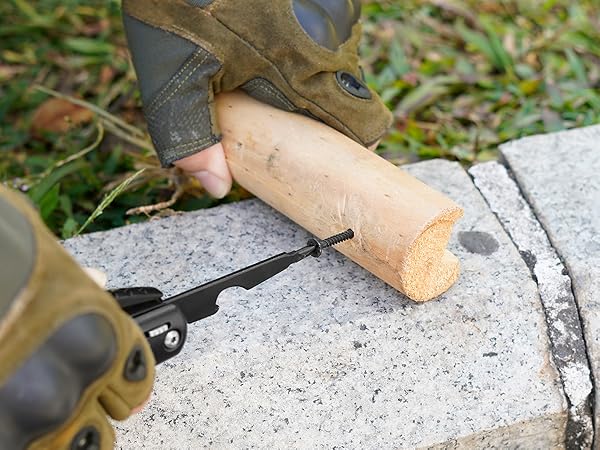 Close-up of hands using pruning shears to cut a wooden stake or dowel on a concrete surface, with grass visible in the background.