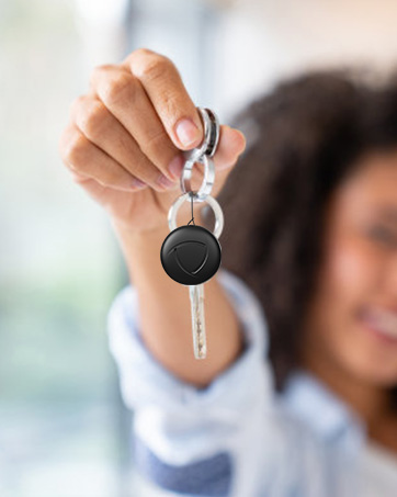 Close-up shot of hand holding up a car key with black electronic fob against blurred background.