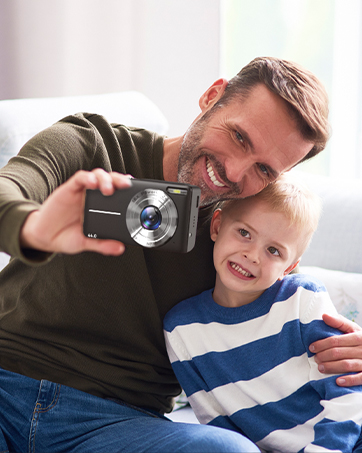 Compact digital camera with prominent lens being held up while taking a selfie-style photo.