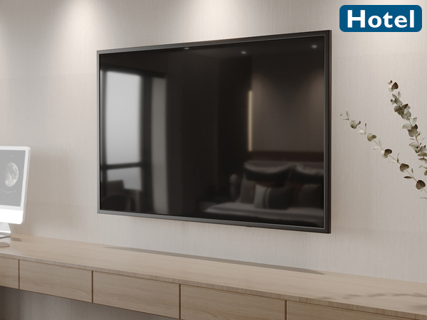 Large wall-mounted flat-screen TV in a hotel room. Wooden desk below with drawers. Plant decoration visible.