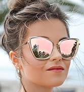 Oversized cat-eye sunglasses with gold frames and pink mirrored lenses worn by a woman with hair in a bun, against a blurred outdoor background.