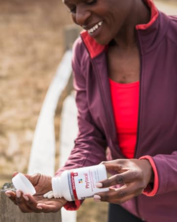 Smiling black woman wearing purple and jacket pink shirt in park pouring supplements into her hand