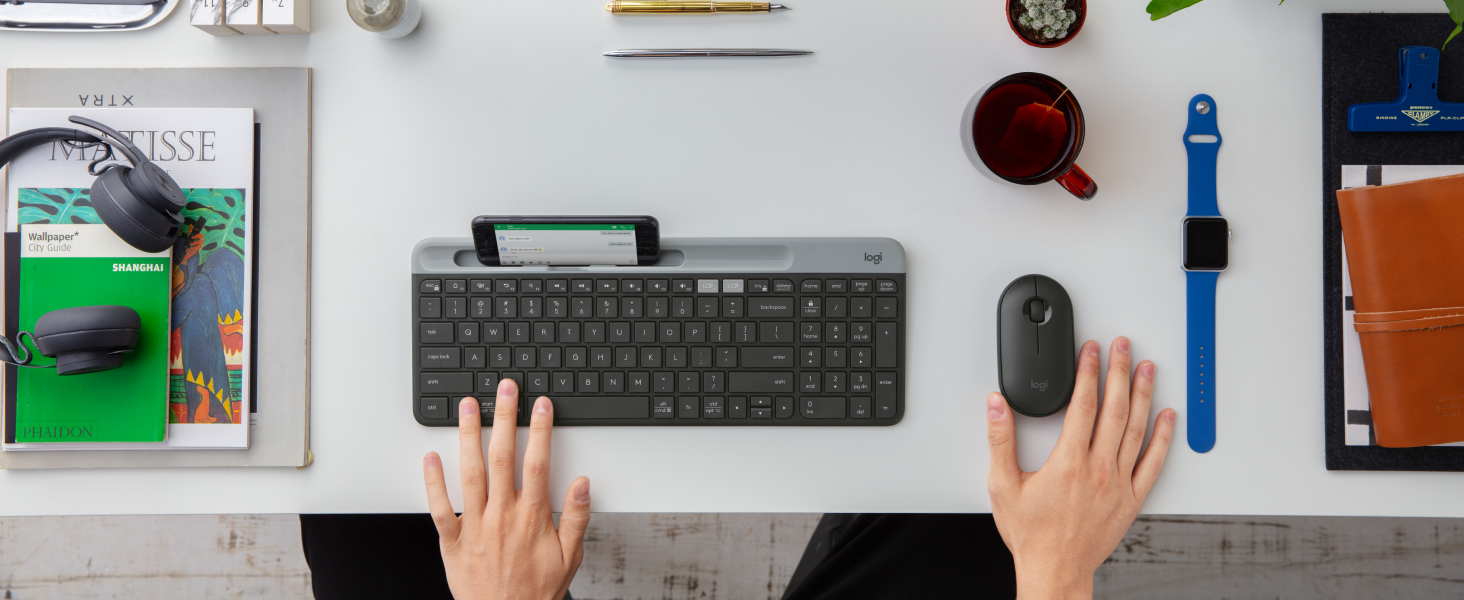 a man using k585 slim compact wireless graphite keyboard with phone holder and m350 cordless mouse