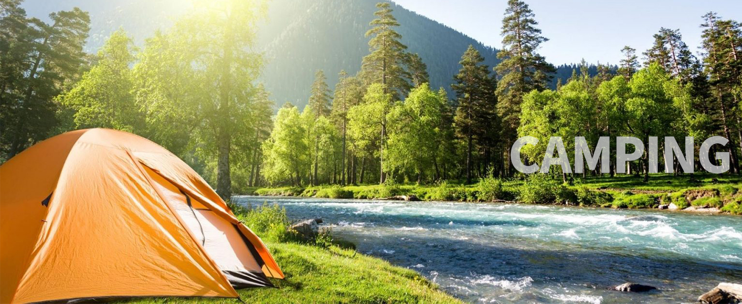 Orange camping tent set up by a rushing river, surrounded by evergreen forest and mountains with sunlight filtering through trees.