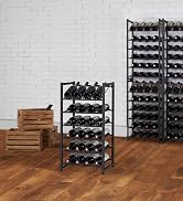 Black metal wine rack holding 24 red wine bottles in brick room and hardwood floor