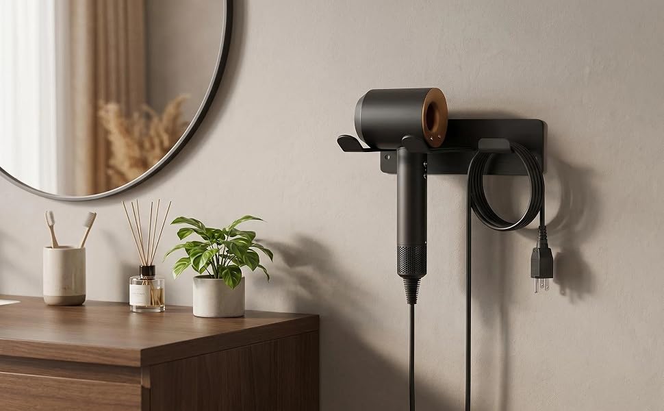 Black handheld hair styling tool mounted on wall beside mirror, with plant and decorative items on shelf below.