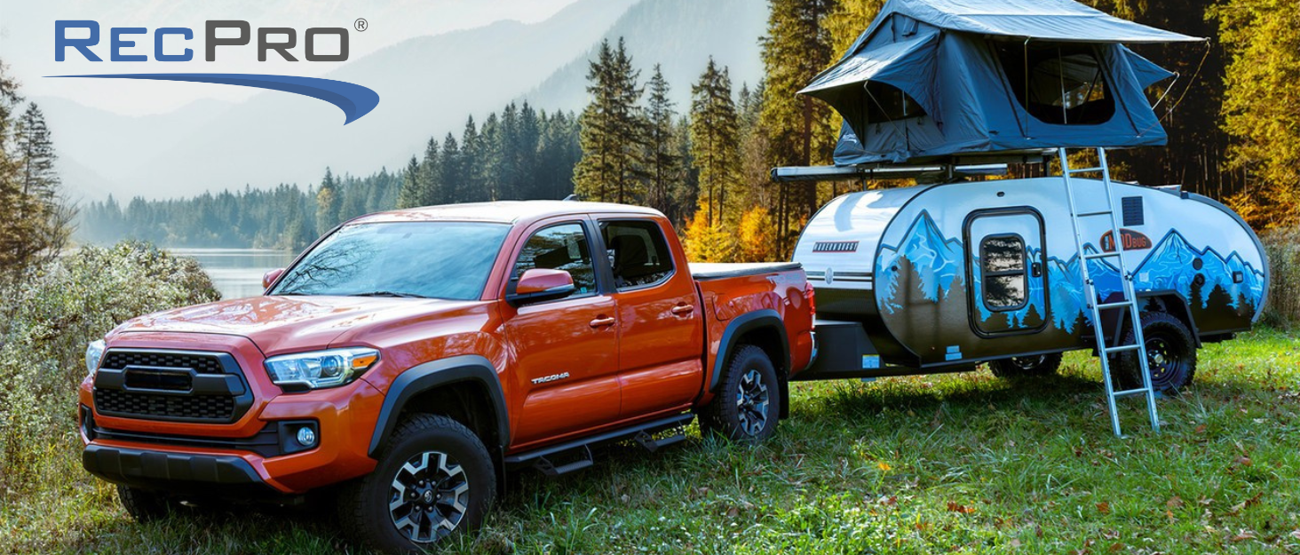 Orange truck pulling mog bug trailer with pop up tent on roof.