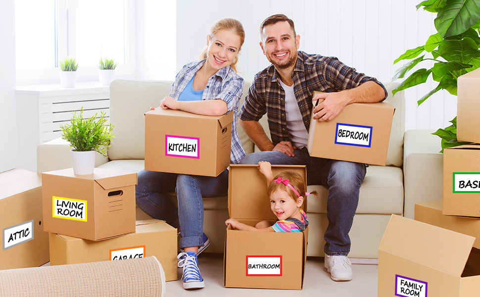 Multiple cardboard moving boxes labeled for different rooms, arranged around a couch with plants in the background, suggesting a home relocation scene.