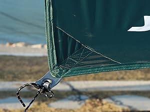 Corner of a dark green tent or canopy. Visible reinforced seam and a black adjustable strap or tie-down.