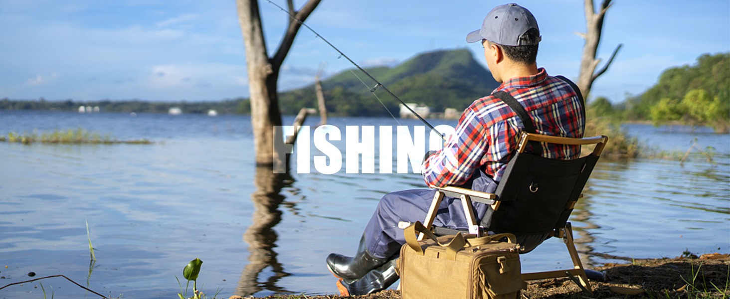 Person in a cap and plaid shirt fishing from a chair by a lake, with trees and hills in the background.