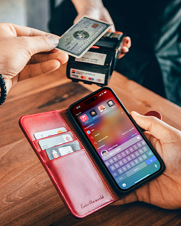 Hands holding a red wallet case with a smartphone displaying a colorful app interface. Another hand holds a credit card above.