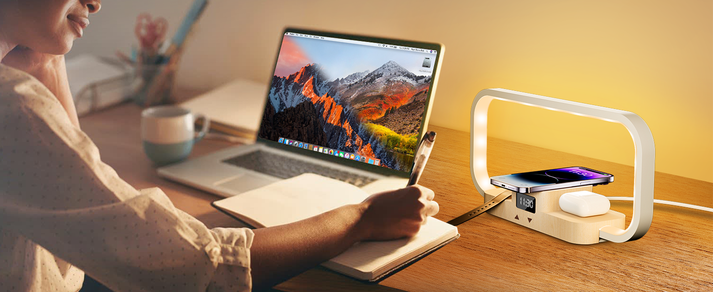 Desk setup with laptop, curved LED lamp, and wireless charging pad. Person's hands visible, working in a home office environment.