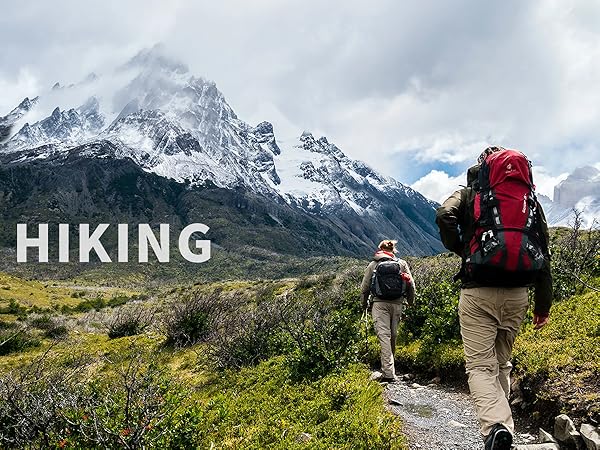 Two hikers on mountain trail with large backpacks. Snowy peaks in background. Text overlay 'HIKING' in white letters.