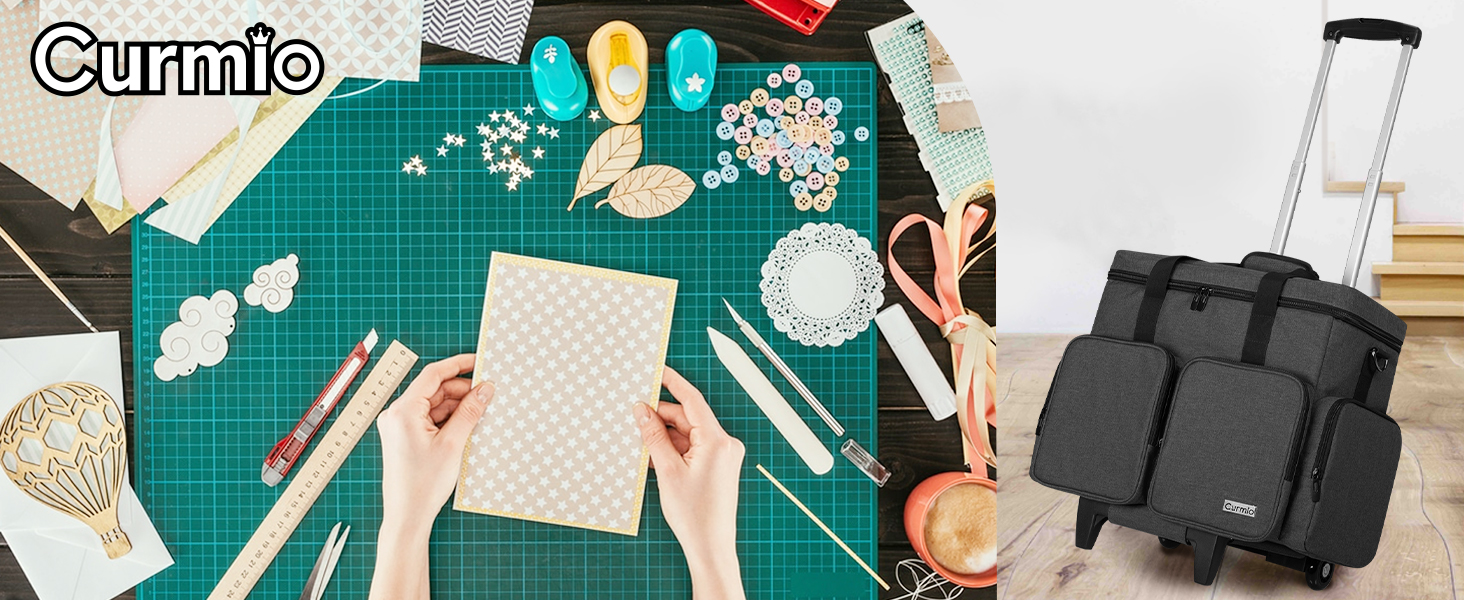 Crafting workspace with green cutting mat, various craft supplies, and a black wheeled trolley bag in the corner.