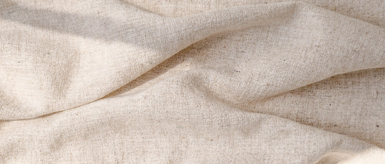 Close-up of folded beige linen fabric with natural texture and soft draping, showing woven material detail.